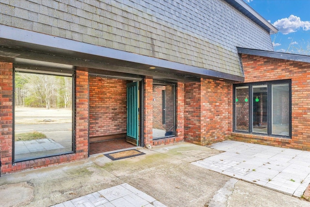 entrance to property with a patio area, brick siding, and roof with shingles