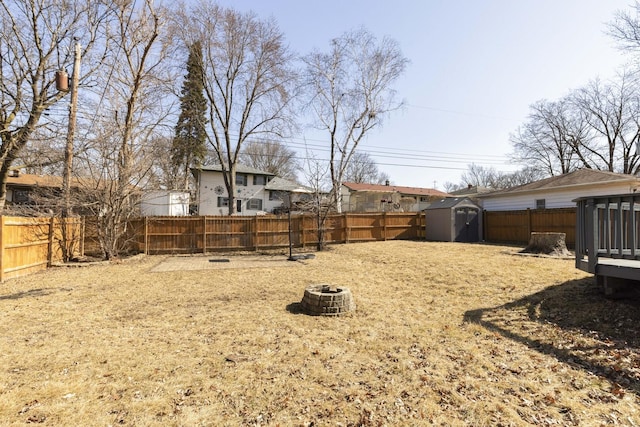 view of yard featuring a storage unit, an outbuilding, a fenced backyard, and an outdoor fire pit