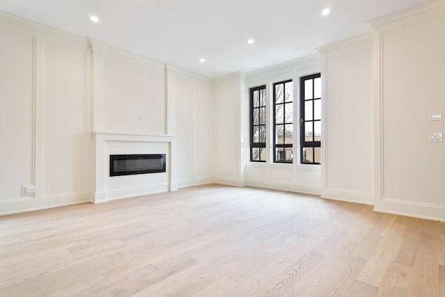 unfurnished living room with a decorative wall, recessed lighting, light wood-style floors, and a glass covered fireplace