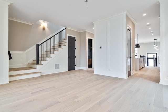 unfurnished living room with light wood-style flooring, ornamental molding, visible vents, and stairs