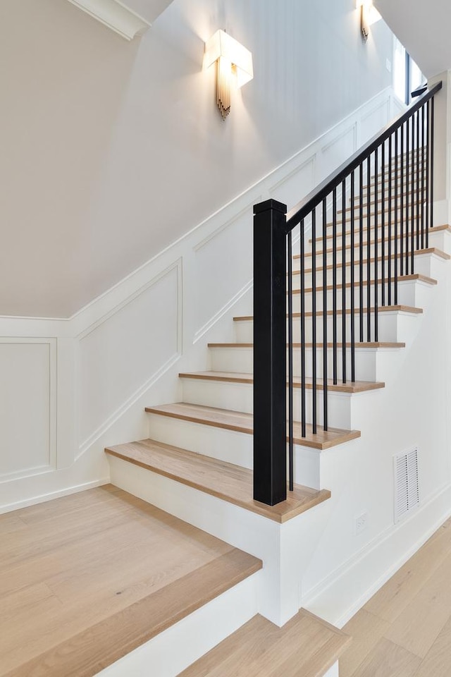stairway with a decorative wall, wood finished floors, wainscoting, and visible vents