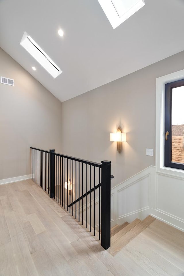 stairway featuring visible vents, recessed lighting, wood finished floors, wainscoting, and lofted ceiling with skylight
