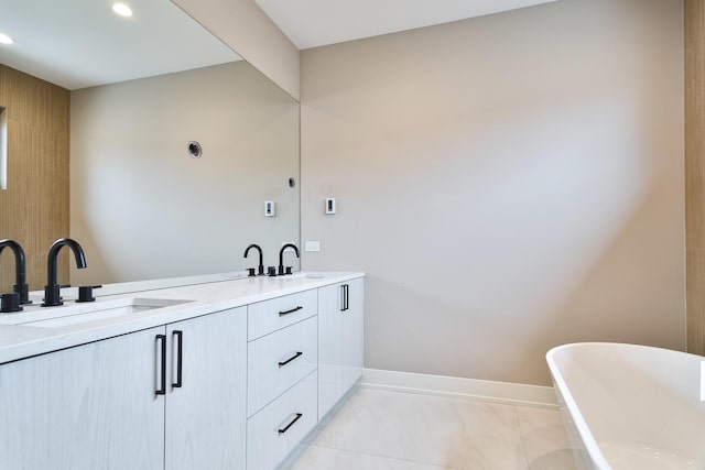 bathroom featuring baseboards, double vanity, recessed lighting, a freestanding bath, and a sink