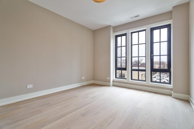 empty room featuring light wood finished floors, visible vents, and baseboards