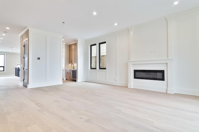 unfurnished living room with a glass covered fireplace, light wood-type flooring, baseboards, recessed lighting, and a decorative wall