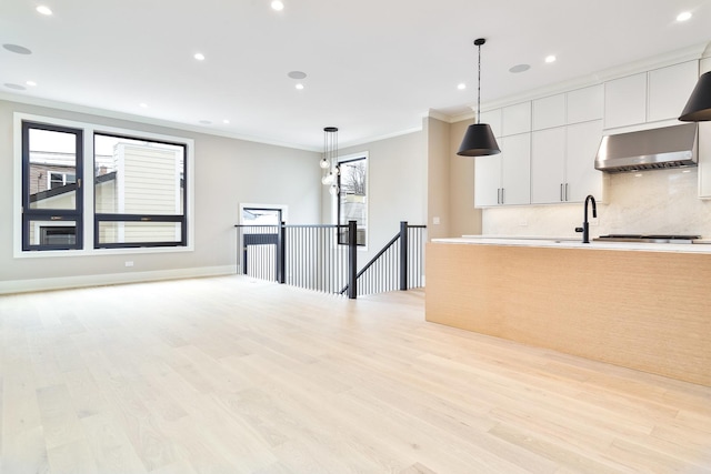 kitchen with tasteful backsplash, decorative light fixtures, ornamental molding, light wood-type flooring, and extractor fan