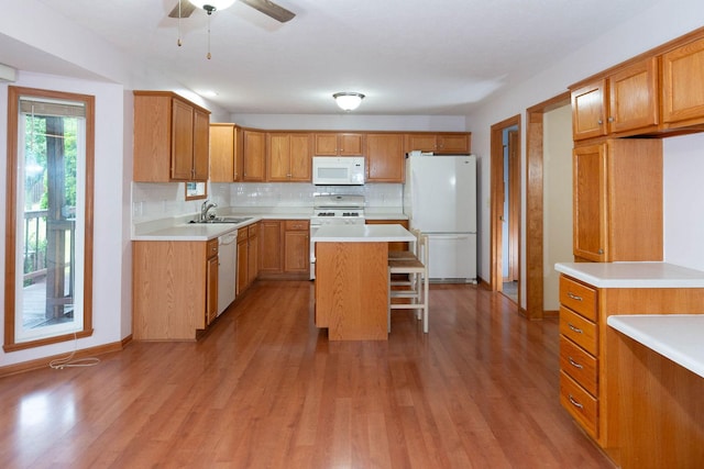 kitchen with decorative backsplash, white appliances, a breakfast bar, and light wood-style flooring