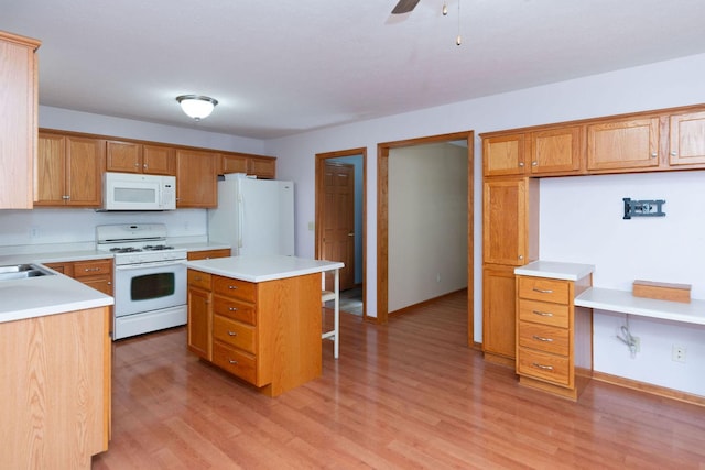 kitchen featuring light wood finished floors, a kitchen island, white appliances, a breakfast bar area, and light countertops