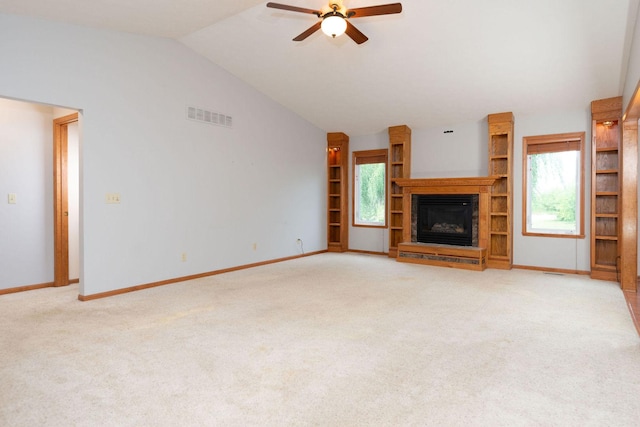 unfurnished living room with visible vents, plenty of natural light, lofted ceiling, and a glass covered fireplace