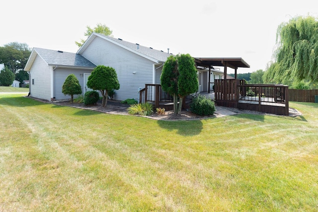 rear view of house featuring a deck, a lawn, and roof with shingles