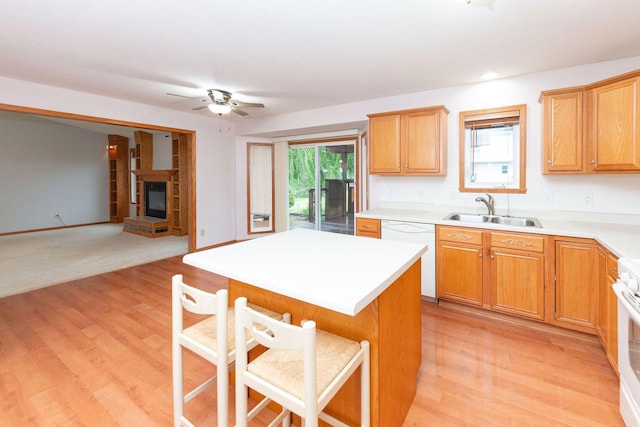 kitchen featuring a sink, a kitchen island, a glass covered fireplace, white appliances, and a breakfast bar area