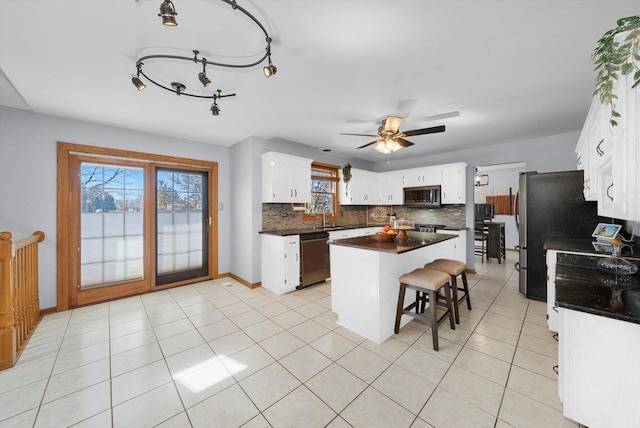 kitchen featuring dark countertops, stainless steel microwave, a center island, dishwasher, and a sink