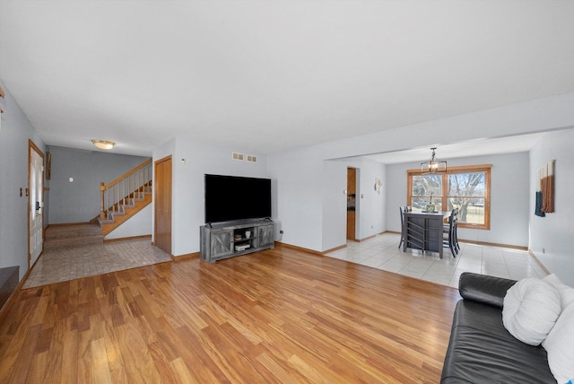 unfurnished living room featuring light wood-type flooring, baseboards, visible vents, and stairs