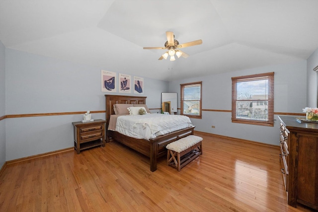 bedroom with lofted ceiling, light wood-style floors, baseboards, and a tray ceiling