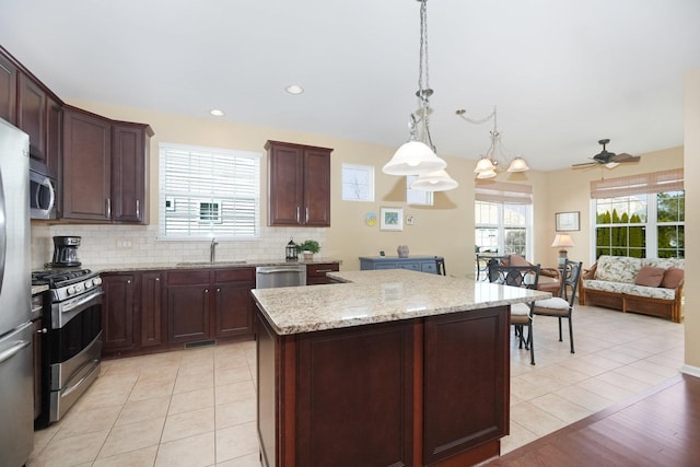 kitchen featuring a center island, light stone countertops, decorative backsplash, stainless steel appliances, and a sink