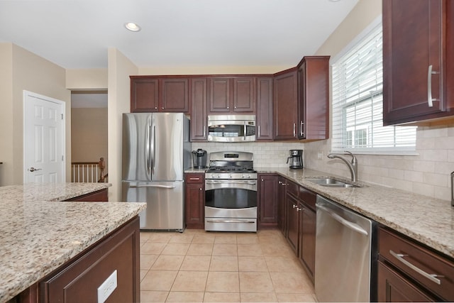 kitchen featuring backsplash, light stone counters, light tile patterned floors, appliances with stainless steel finishes, and a sink