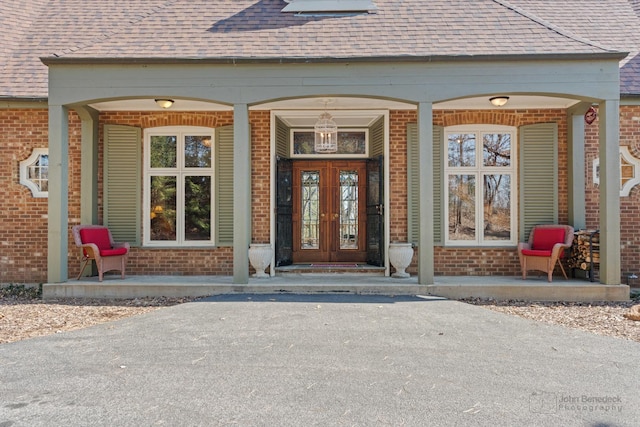 entrance to property featuring brick siding, covered porch, and french doors