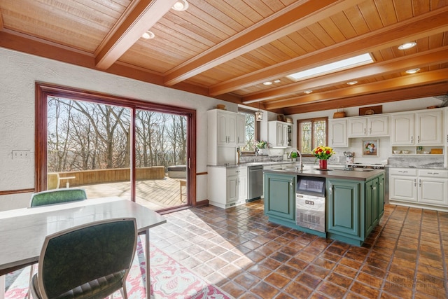 kitchen with a skylight, white cabinets, stainless steel dishwasher, and green cabinetry