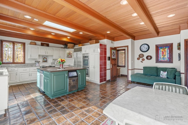 kitchen featuring beamed ceiling, stainless steel appliances, a skylight, white cabinets, and green cabinetry