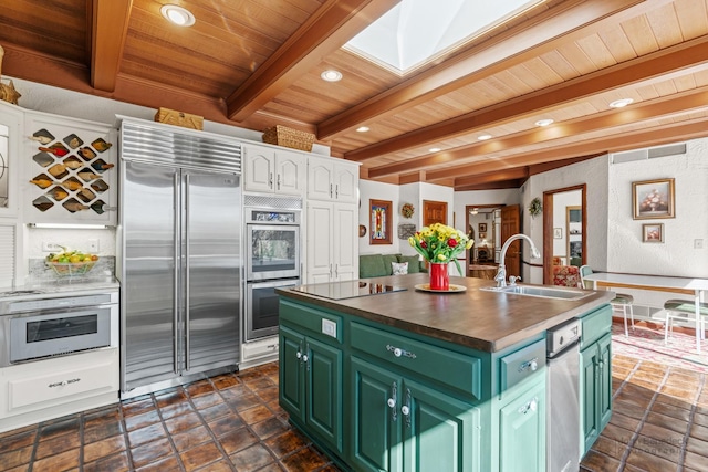 kitchen with green cabinetry, beam ceiling, stainless steel appliances, white cabinetry, and a sink