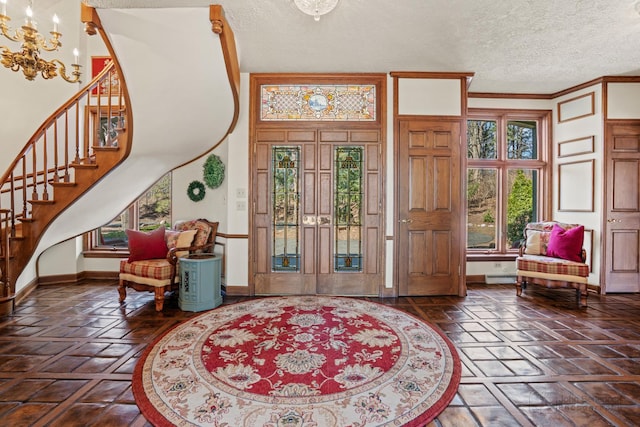 entrance foyer featuring baseboards, ornamental molding, stairs, a textured ceiling, and a chandelier