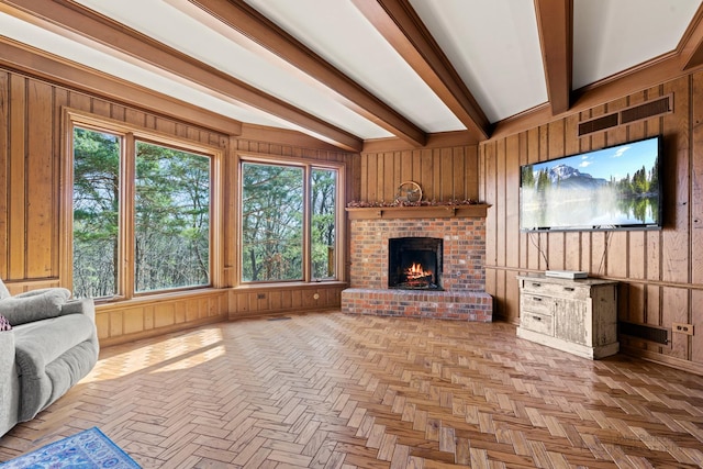 unfurnished living room with a brick fireplace, wooden walls, visible vents, and beamed ceiling