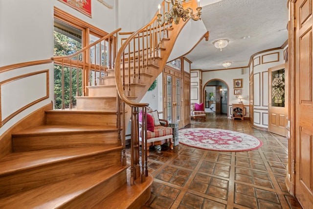 foyer entrance with arched walkways, stairway, a textured ceiling, and ornamental molding