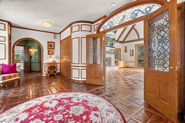 foyer entrance with a textured ceiling, a fireplace with raised hearth, arched walkways, and ornamental molding