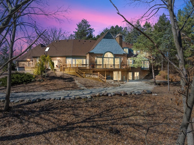 back of house featuring brick siding, stairway, a chimney, and a deck