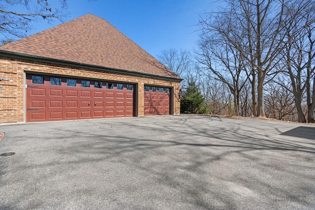 view of side of home featuring an outbuilding, brick siding, and a shingled roof