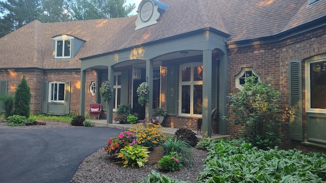 view of front of home featuring brick siding, covered porch, driveway, and roof with shingles