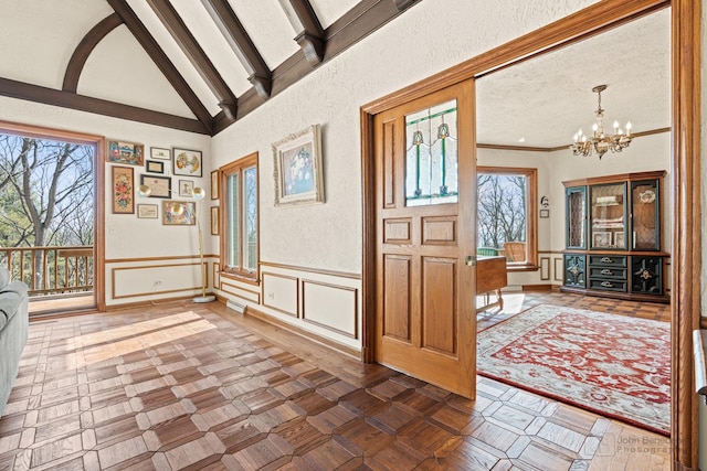 entrance foyer featuring lofted ceiling with beams, a chandelier, a wealth of natural light, and a textured ceiling