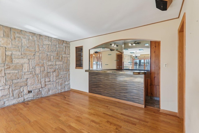 interior space with baseboards, arched walkways, wood finished floors, and crown molding