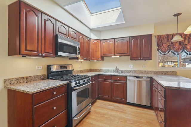 kitchen featuring light wood-style flooring, a sink, stainless steel appliances, light stone countertops, and hanging light fixtures