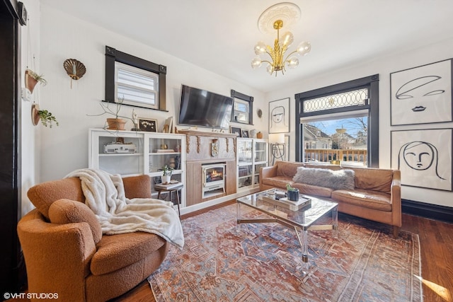 living area featuring a lit fireplace, an inviting chandelier, and wood finished floors