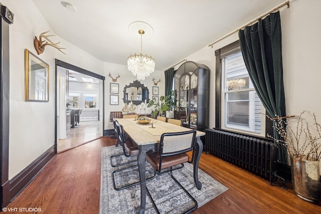 dining room with dark wood finished floors, an inviting chandelier, radiator heating unit, and a healthy amount of sunlight