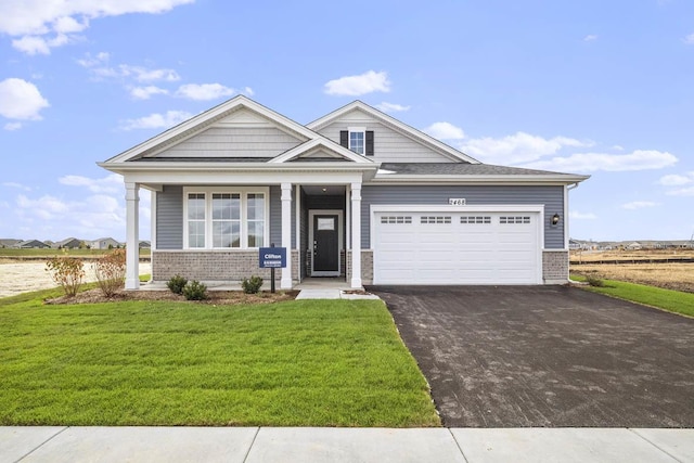 craftsman house with aphalt driveway, a garage, brick siding, and a front lawn