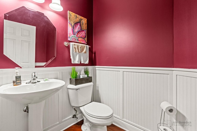 half bath featuring toilet, wood finished floors, a wainscoted wall, and a sink