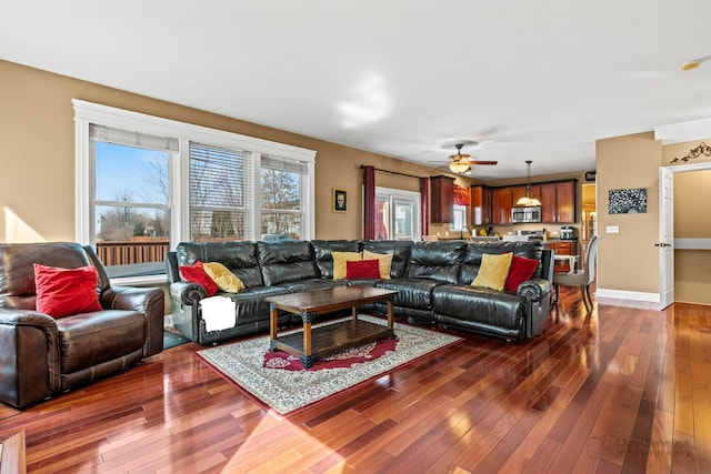 living room with baseboards, dark wood-type flooring, and a ceiling fan