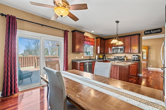 kitchen featuring a kitchen island, baseboards, dark wood-style floors, stainless steel appliances, and a sink