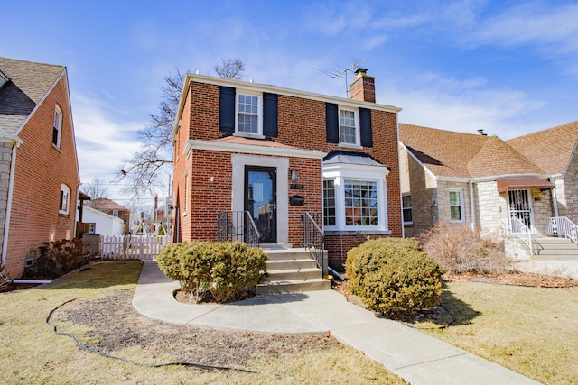 view of front of home featuring brick siding, a chimney, and fence