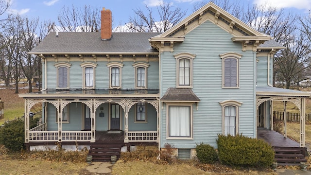 italianate-style house featuring a porch, roof with shingles, and a chimney