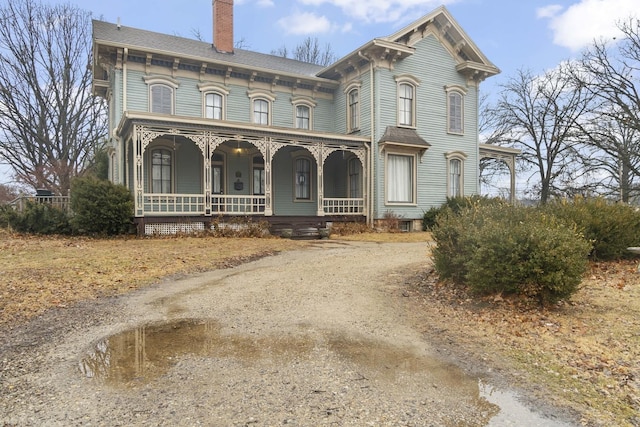 italianate house with covered porch, a chimney, and dirt driveway