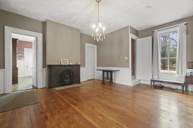 unfurnished living room with a chandelier, a wainscoted wall, a fireplace, and hardwood / wood-style floors