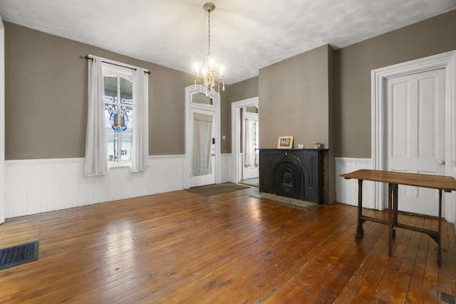 unfurnished living room featuring visible vents, a wainscoted wall, hardwood / wood-style floors, an inviting chandelier, and a fireplace