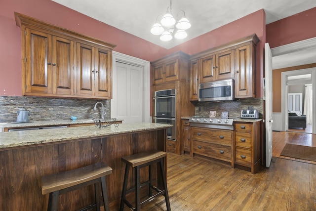 kitchen featuring a kitchen breakfast bar, light stone countertops, dark wood-style flooring, and appliances with stainless steel finishes