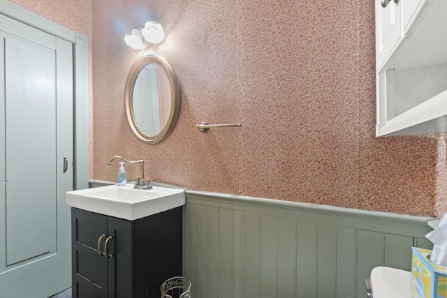 bathroom with wallpapered walls, toilet, vanity, and a wainscoted wall
