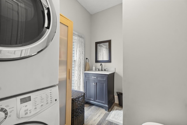 washroom with a sink, wood finished floors, laundry area, and stacked washer / dryer