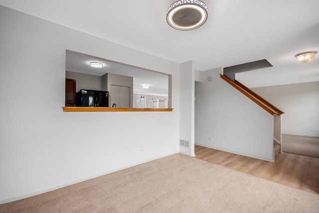 unfurnished living room featuring visible vents, wood finished floors, stairs, and carpet floors