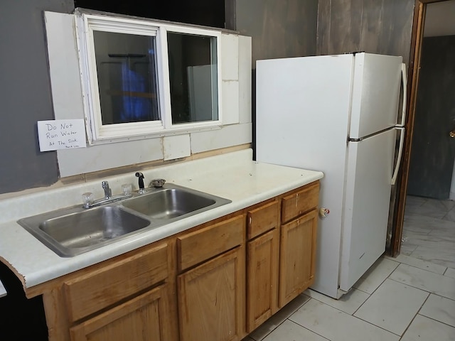 kitchen with light countertops, brown cabinetry, freestanding refrigerator, and a sink